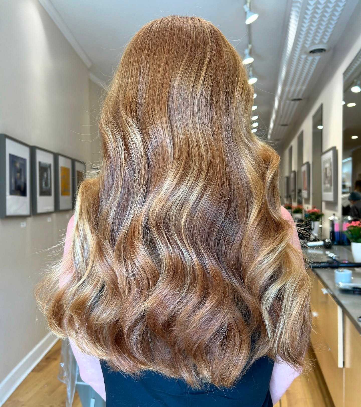 Wavy golden brown hair in a salon, framed by wall art and mirrors.