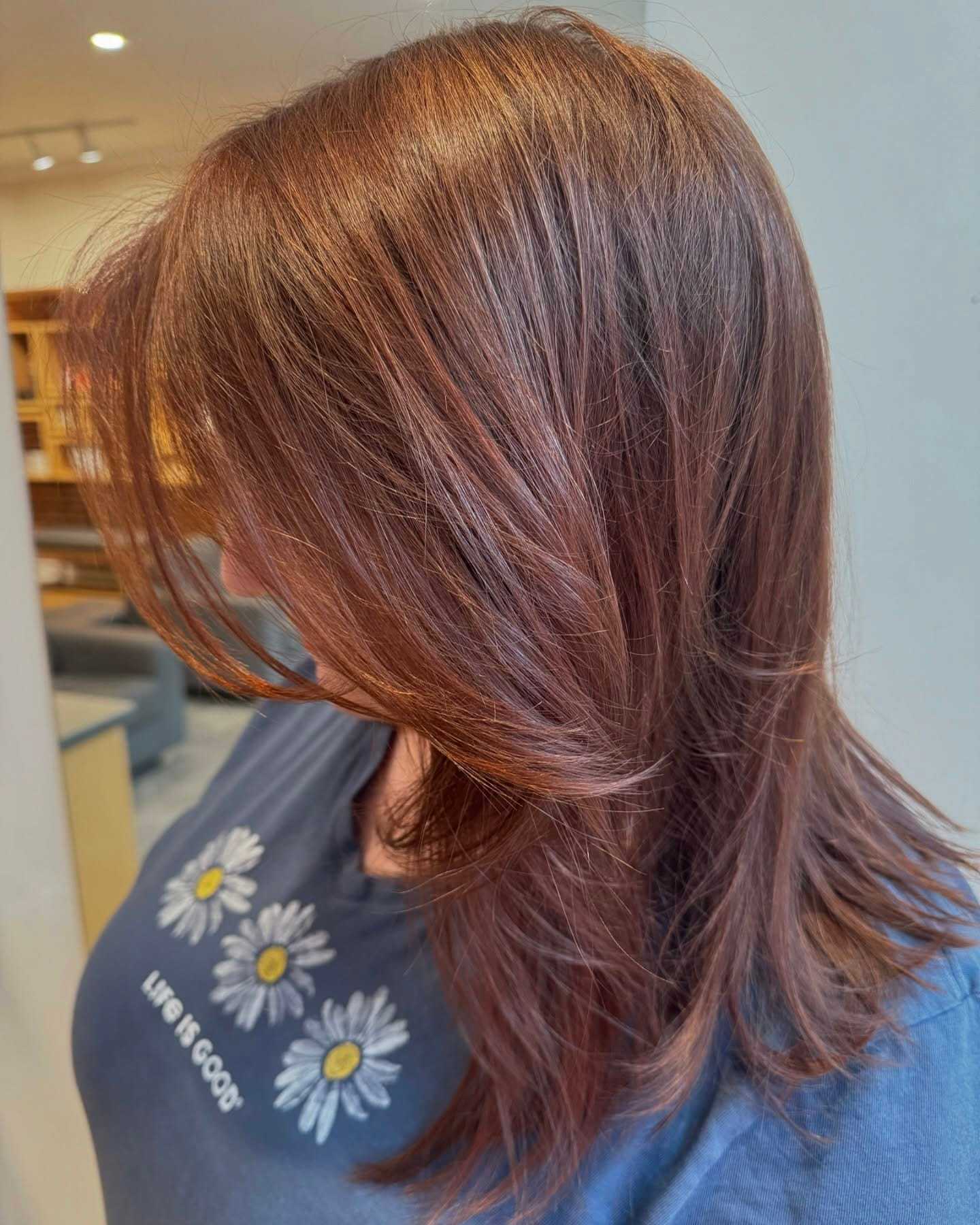 Woman with layered brown hair, wearing a daisy-printed shirt in a salon.