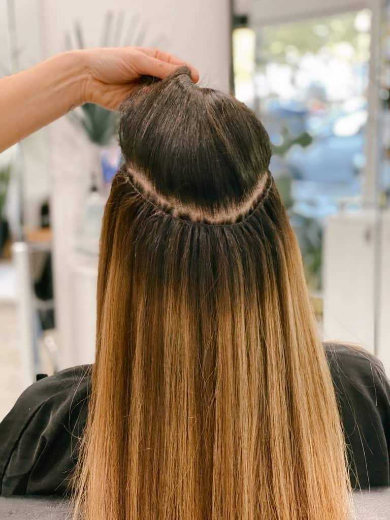 Hair extension application on brown hair, hand holding top section for styling.