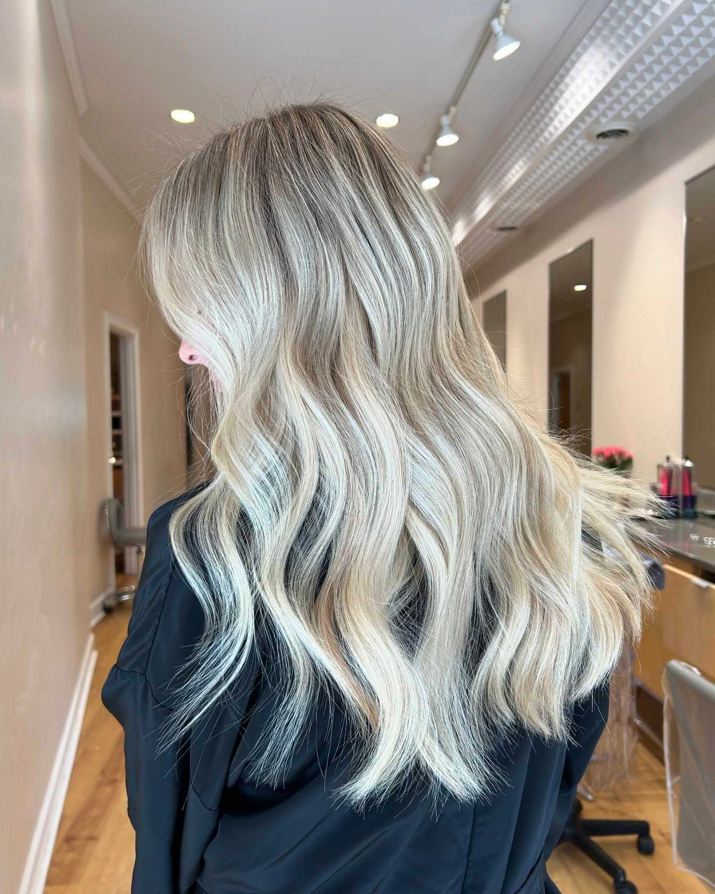 Long blonde wavy hair in a salon setting, with elegant lighting and mirrors.